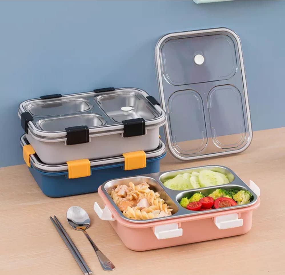 Three compartment lunchboxes with food, including pasta, cucumber, tomatoes, and broccoli, are stacked on a table beside a spoon and chopsticks.